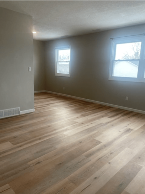 an empty living room with wood flooring and two windows